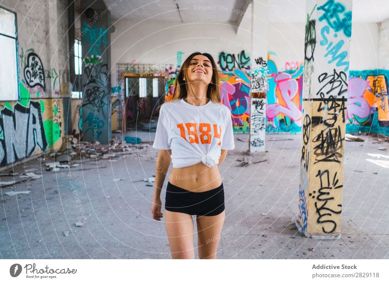 Lächelnde Frau in verlassenem Raum mit Graffiti heiter Körperhaltung Blick in die Kamera Glück Jugendliche schäbig mehrfarbig hübsch lässig Verlassen Gebäude
