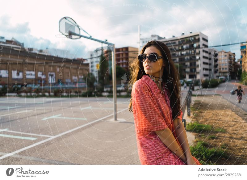 Frau, die auf dem Spielplatz in einem Zaun sitzt. Stil Straße Stadt Körperhaltung Sonnenbrille Porträt attraktiv Beautyfotografie trendy Lifestyle hübsch Mode