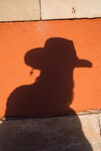 Männlicher Schatten mit Pistole an der Wand Mann Cowboy Westen Silhouette wild Western Umrisslinie Hut hell Risiko Sonnenlicht Kontrast gefährlich Stil