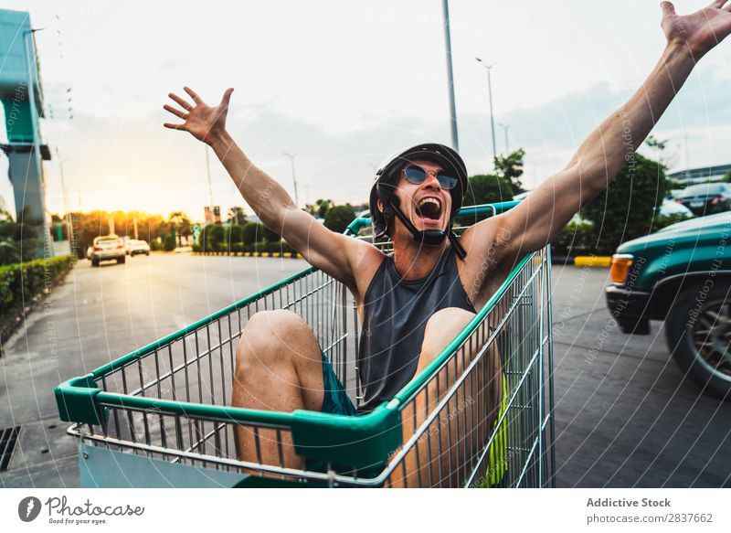 Emotionaler Mann im Warenkorb kaufen Handwagen Reiten Karre Schiebkarre Sonnenbrille Käufer Ausritt gutaussehend heiter Freude Parkplatz Mensch Markt Humor
