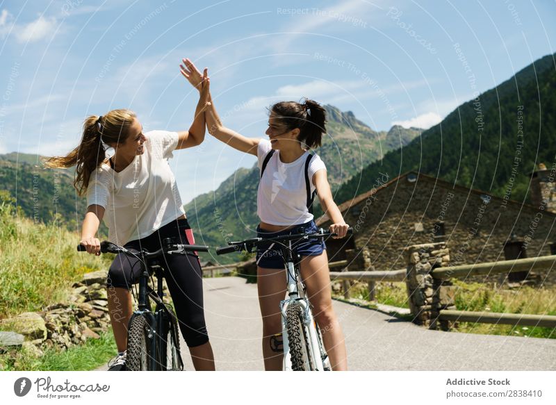 Frauen auf Fahrrädern, die High Five geben. sportlich Fahrrad high five Lächeln heiter Team Freundschaft Sport Zyklus Mädchen Aktion Lifestyle Fahrradfahren