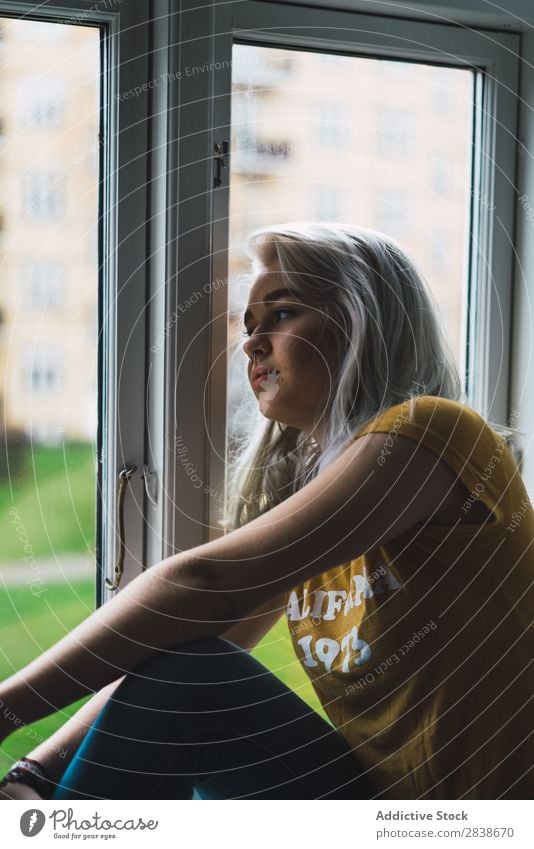 Nachdenkliche blonde Frau am Fenster hübsch heimwärts Jugendliche sitzen Fürsorge aussruhen schön Lifestyle Beautyfotografie attraktiv Wegsehen Porträt Dame