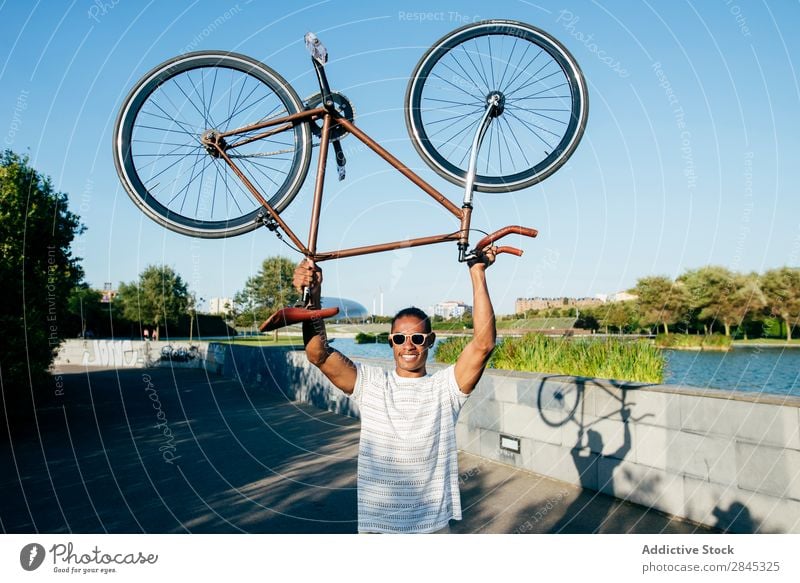 Fröhlicher Mann mit Fahrrad Halt heiter über Kopf Jugendliche schwarz lässig stehen Großstadt Mensch Lifestyle sportlich Sport Fahrradfahren Körperhaltung Glück