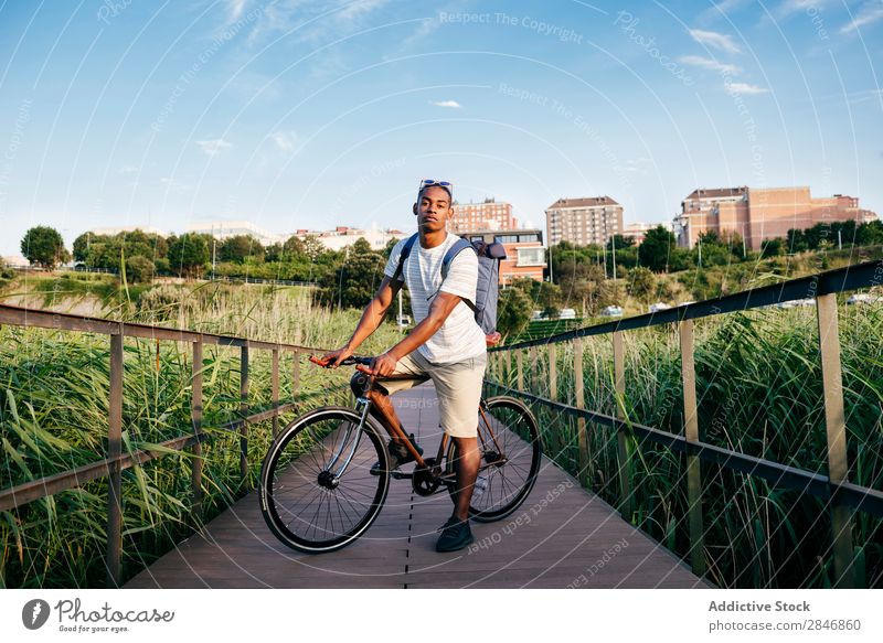 Junger Mann, der mit dem Fahrrad auf dem Bürgersteig posiert. Straßenbelag Gras Brücke Geländer Lifestyle Verkehr Stadt Zyklus Großstadt Aktion Gasse