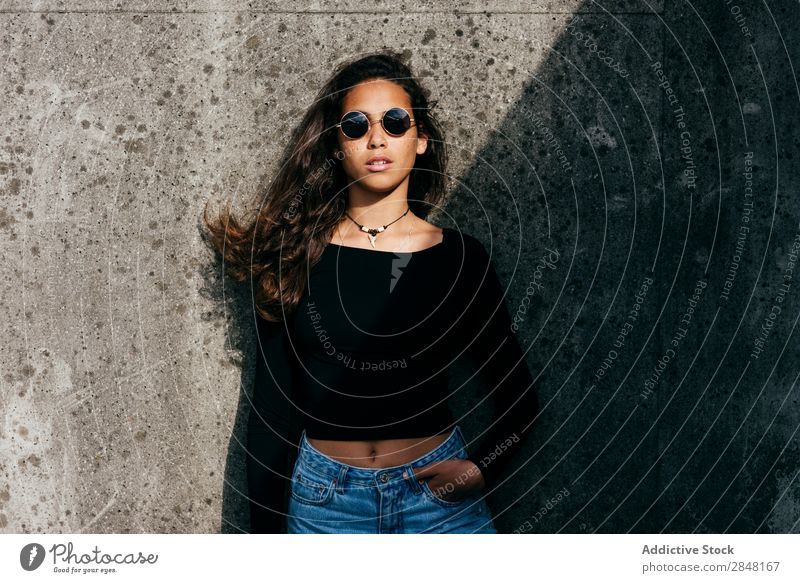 Charmanter Teenager im Sonnenlicht Frau Stadt Stil Bekleidung selbstbewußt Jugendliche Sonnenbrille Schickimicki lockig Hände in den Taschen Körperhaltung