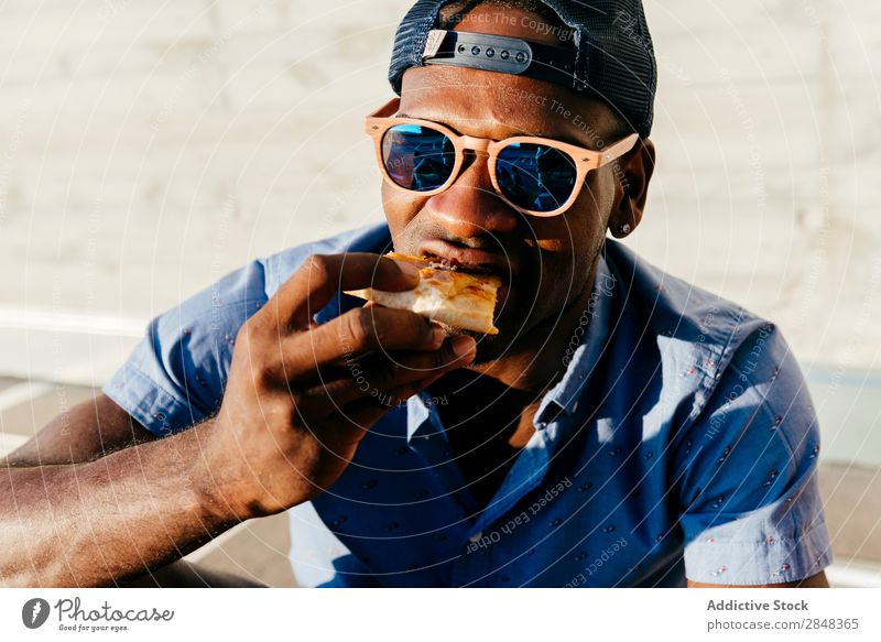 Junger schwarzer Mann isst Pizza auf der Straße Stil Porträt genießend Lebensmittel Mittagessen Lifestyle Schüler trendy gutaussehend Jugendliche selbstbewußt