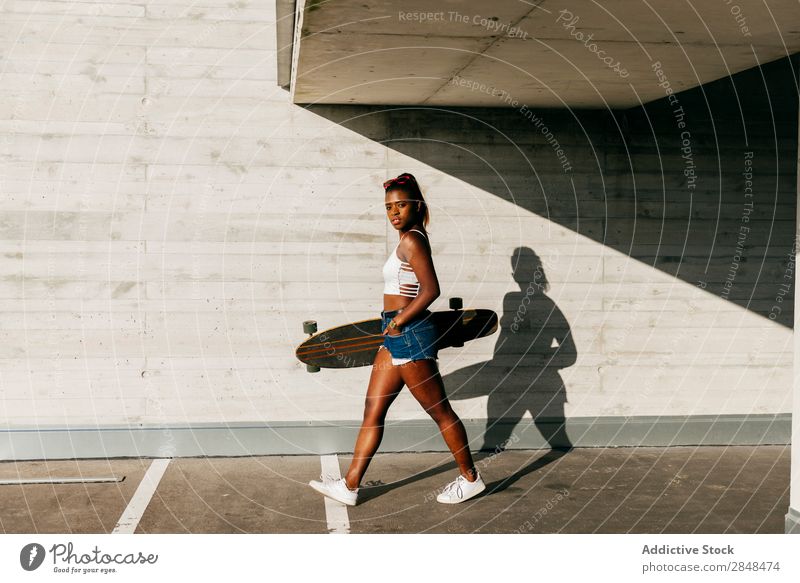 Stilvolle Frau mit Brett, die auf der Straße spazieren geht. Longboard Stadt Sport Freizeit & Hobby Skateboarderin schwarz Skateboarding Jugendliche Afrikanisch