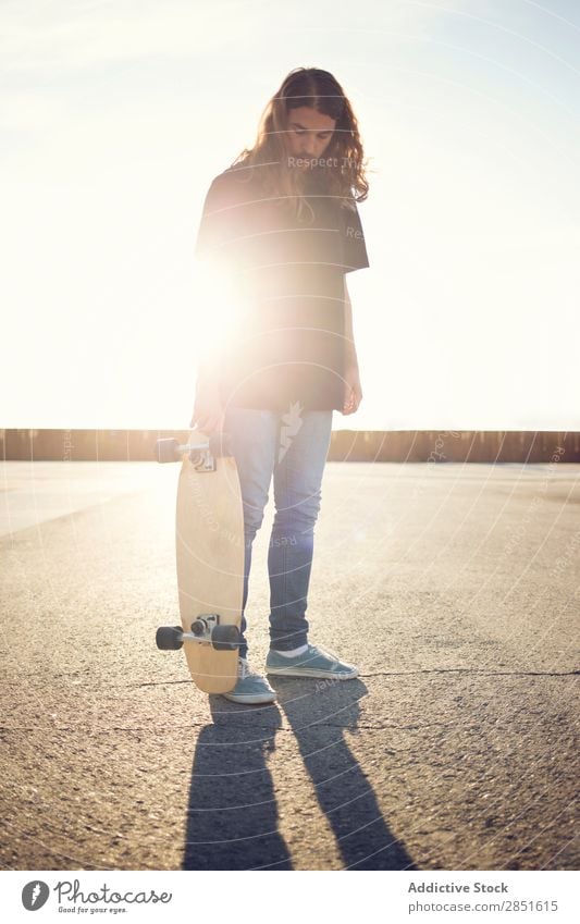 Mann posiert mit Skateboard am Abend Skateboarding Schlittschuhlaufen lange Haare Quadrat Asphalt Sonnenuntergang Skateboarderin Jugendliche Lifestyle Freude