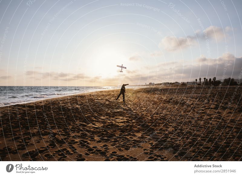 Ein unkenntlicher Mann an einem Strand, der das Spielzeugflugzeug wirft. Mensch Flugzeug Spielen werfen Etage Glück Freude Lifestyle träumen kindisch Abend