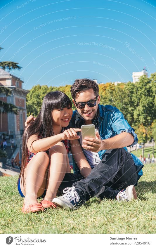 Junges glückliches Paar mit Smartphones im Park asiatisch schön Freund lässig Solarzelle Handy Chinese Mitteilung Verbindung Textfreiraum Europa Frau