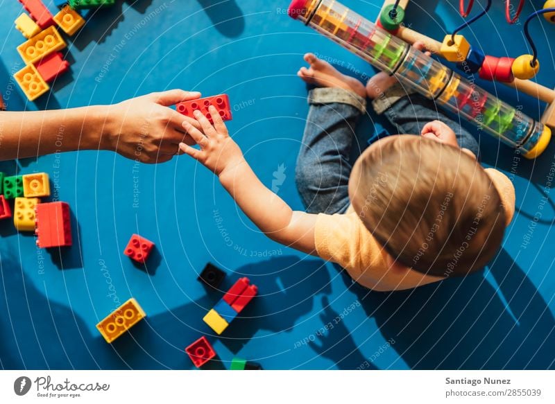 Frohes Baby beim Spielen mit Spielzeugblöcken. Kinderbetreuung Kindergarten Schule Mutter Lehrer Hilfsbereitschaft Mama Kleinkind Junge klein LEGO Glück