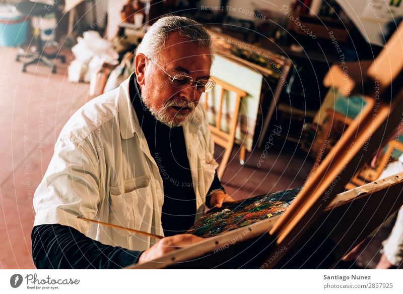Alter Mann Künstler beim Malen von Ölen in seinem Atelier. Erwachsene Vollbart Maler konzentriert Gemälde Pinsel Bürste Staffelei Leinwand Konzentration