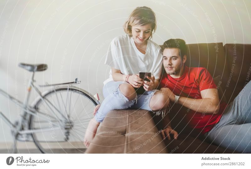 Koppelung auf dem Sofa auf dem Handy Paar heimwärts Zusammensein Glück sprechen interagierend Lächeln Kaffee Liebe Mensch Lifestyle Jugendliche lässig