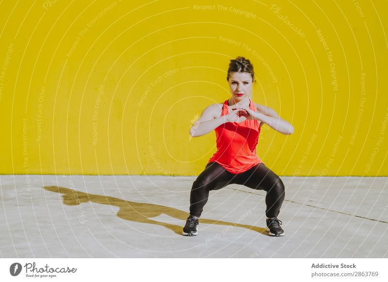 Frau macht Gruppenübungen in der Nähe einer gelben Wand. Truppe üben Sportbekleidung sportlich Jugendliche Fitness Training Presse Dame Gerät Kraft dünn stark