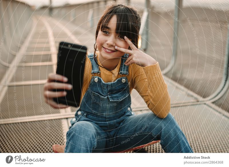 Lustiges Mädchen nimmt Selfie auf dem Smartphone auf dem Laufsteg. Jugendliche Selfie nehmen PDA Gang konfrontierend Jeansoverall Fußweg lustig Großstadt Stil