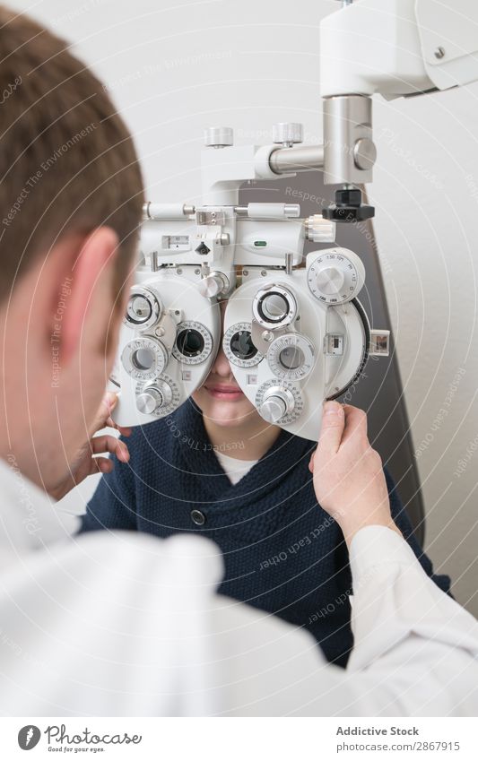 Optiker testet die Augen eines Jungen Kind Klinik Gerät diagnostizieren Anzeige Arzt Prüfung & Examen Brillenträger Gesundheit Krankenhaus Hygiene Medikament