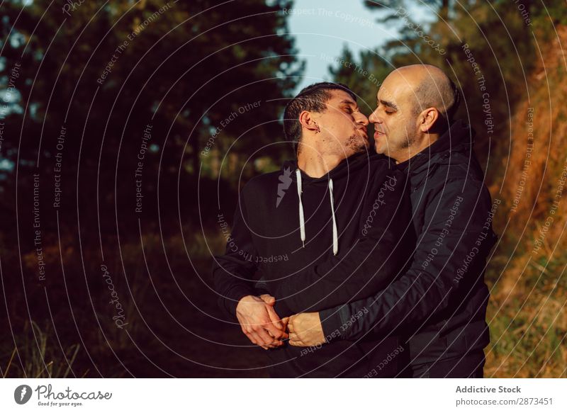 Lächelnde Männer, die sich auf dem Weg im Park umarmen. Homosexualität Paar Umarmen Liebe Wege & Pfade Wald umarmend Schönes Wetter geschlossene Augen heiter