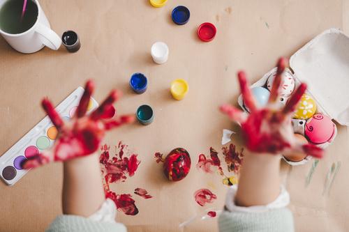 Kind zeigt schmutzige Hände in der Nähe von Hühnereiern und Farben am Tisch. Hand Ostern Ei dreckig zeigen malen Handfläche Hähnchen Container Frühling Kulisse