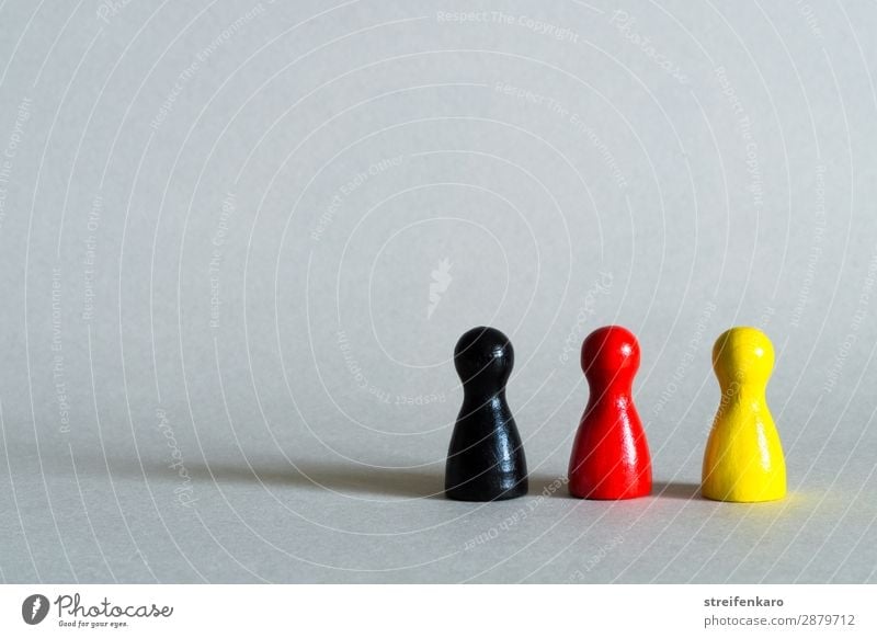 Drei Spielfiguren in schwarz, rot, gelb stehen in einer Reihe Menschengruppe Spielzeug Holz Zeichen Zusammensein Gesellschaft (Soziologie) Politik & Staat