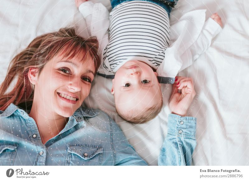 glückliche junge Mutter und ihr kleiner Junge liegen auf dem Bett und lächeln. Lifestyle Freude Glück Haut Lampe Schlafzimmer Kind Mensch maskulin feminin Baby