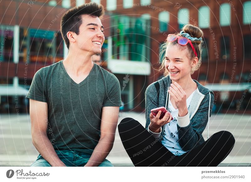 Ein befreundetes Paar, ein Mädchen und ein Junge im Teenageralter, die sich gemeinsam mit Smartphones amüsieren, im Stadtzentrum sitzen und Zeit miteinander verbringen