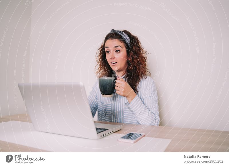 Eine Frau sieht überrascht auf ihren Laptop, während sie einen Becher hält. Kaffee Lifestyle Glück Schreibtisch Tisch Arbeit & Erwerbstätigkeit Büro Business