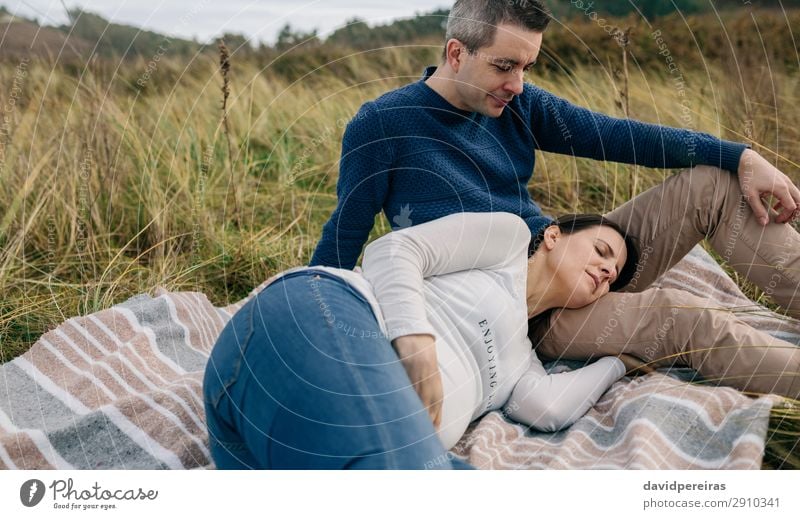 Mann sieht seine schwangere Frau an, die auf dem Gras ruht. Lifestyle Erholung Mensch Baby Erwachsene Vater Familie & Verwandtschaft Paar Natur Landschaft