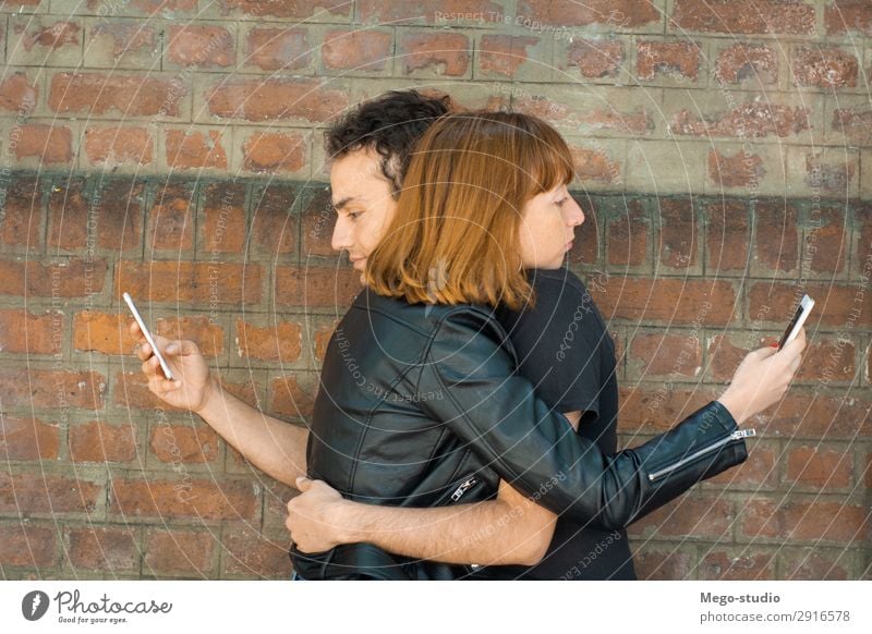 Ein junges Paar, das sich umarmt, während jeder auf sein eigenes Smartphone starrt. Lifestyle Glück schön Telefon PDA Technik & Technologie Internet Mensch Frau
