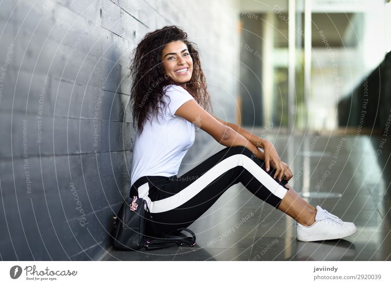 Fröhliche arabische Frau, schwarze lockige Frisur, die auf dem städtischen Boden sitzt. Lifestyle Stil Glück schön Haare & Frisuren Gesicht Sport Mensch feminin