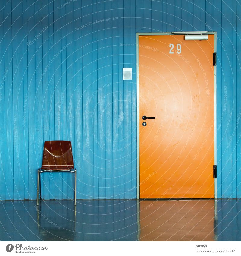 orangene Tür mit Nummer 29 und Türschild in blauer Wand und einem Stuhl für Wartende  davor. Büro Klassenraum Flur Eingang Ziffern & Zahlen warten ästhetisch