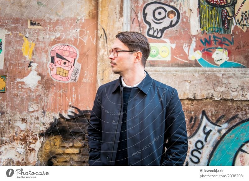 Portrait eines jungen Mannes vor einer Wand Italien Rom Porträt Junger Mann Straßenkunst Mantel Profil Zurückblicken Blick Brillenträger Totenkopf Graffiti