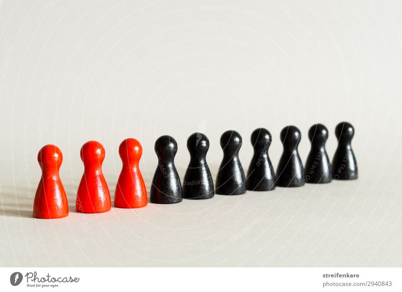 Drei rote Spielfiguren stehen mit sieben schwarzen Spielfiguren in einer Reihe Menschengruppe Spielzeug Holz ästhetisch einfach Kraft gewissenhaft Wahrheit