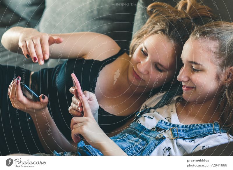 Junge Frauen, die Mobiltelefone benutzen, Musikclips anschauen, SMS und Nachrichten schreiben. Teenager, die die Smartphones benutzen und zu Hause auf dem Sofa sitzen. Benutzen technische Geräte. Mädchen tragen Sommerkleidung