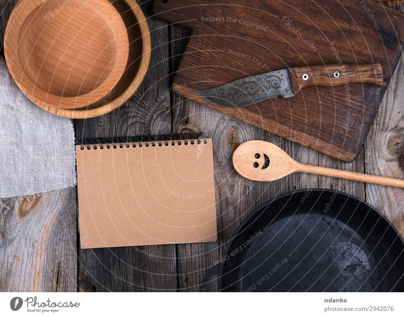 leere schwarze runde Bratpfanne, Schneidebrett Teller Pfanne Messer Löffel Tisch Küche Papier Holz Metall alt oben Sauberkeit braun grau Hintergrund Holzplatte