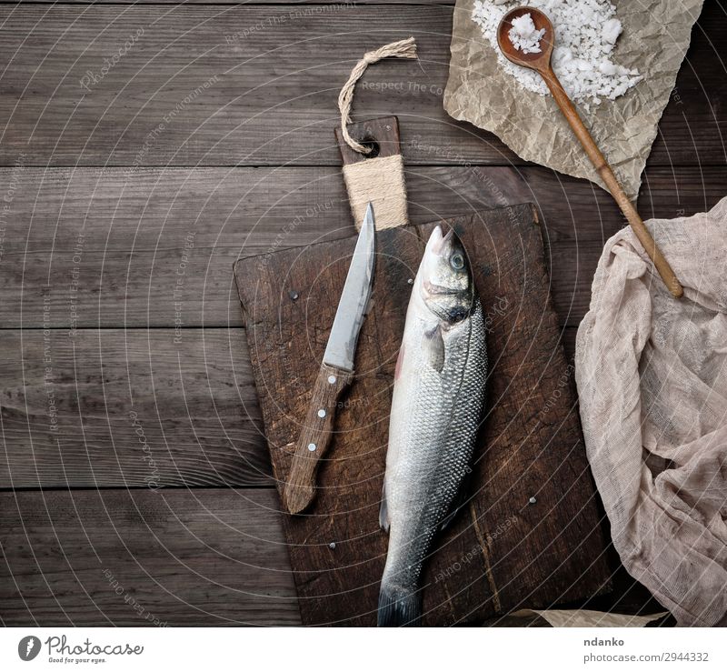 frischer ganzer Seebarschfisch Fisch Meeresfrüchte Ernährung Löffel Küche Tier Stoff Papier Holz oben braun grau Bass Holzplatte Essen zubereiten Schneidebrett