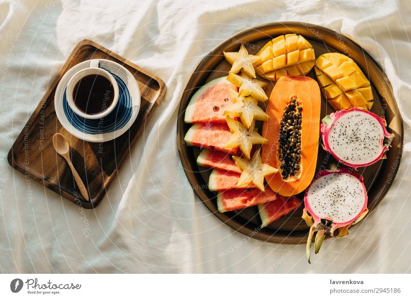 Kaffee oder Tee und tropische Obstplatte auf weißem Bett Schlafzimmer Getränk Frühstück Karambole Tasse Drachenfrucht exotisch Flachlegung Gesunde Ernährung