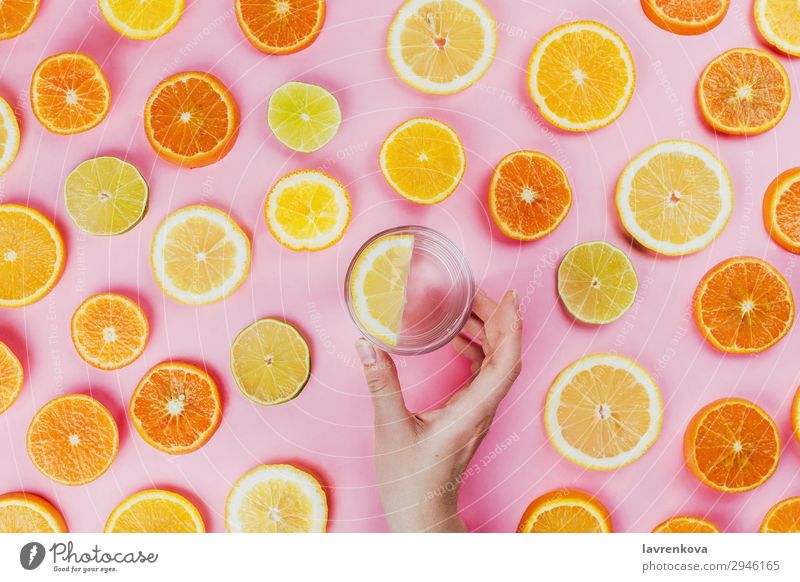 Frauenhand mit Zitronenwasser und geschnittenen Zitrusfrüchten rosa flache Verlegung freches Wasser Halt Hand Limone rund Diät Vegetarische Ernährung