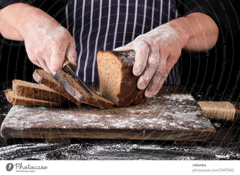 Koch in schwarzer Uniform hält ein Küchenmesser. Brot Ernährung Essen Mittagessen Abendessen Messer Tisch Mann Erwachsene Hand Holz dunkel frisch lecker