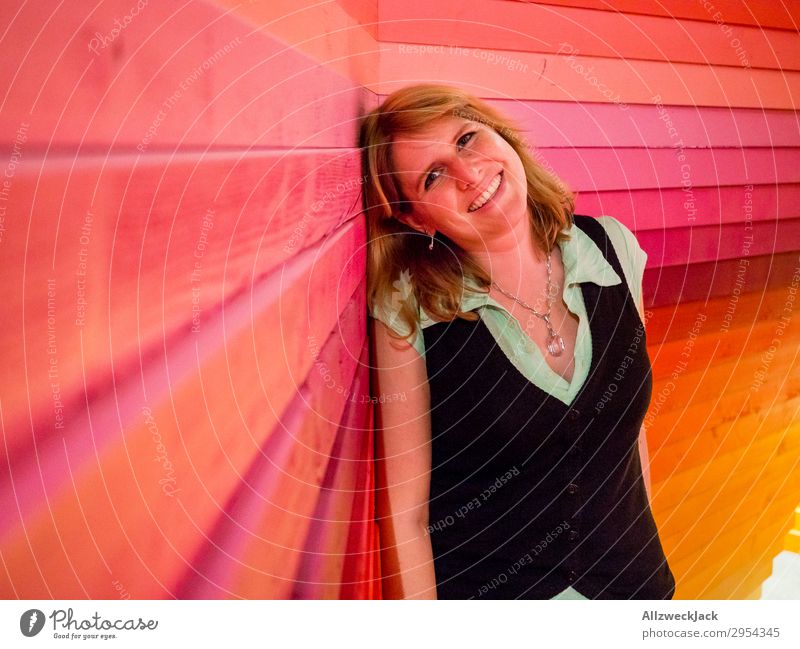 junge Frau lehnt glücklich an einer bunten Holzwand Innenaufnahme 1 Mensch Junge Frau Kunstlicht Porträt Blick nach vorn Blick in die Kamera blond Zaun Barriere