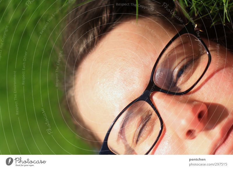 Gesicht einer Frau mit Brille im Gras. Augen halb geschlossen. Blinzeln im Sonnenlicht. Erholen und entspannen feminin Junge Frau Jugendliche Erwachsene Kopf