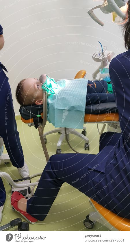Ein Fragment eines Zahnarztzimmers mit einem Kind, das auf einem Zahnarztstuhl liegt, und einem Teil der Figur des Arztes Behandlung Arbeit & Erwerbstätigkeit