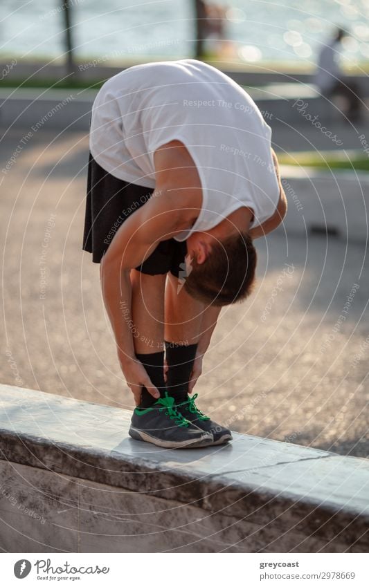 Ein Jugendlicher streckt sich, zieht den Kopf auf die Knie, im Freien Sport Leichtathletik Sportler Yoga maskulin Junger Mann 1 Mensch 13-18 Jahre T-Shirt