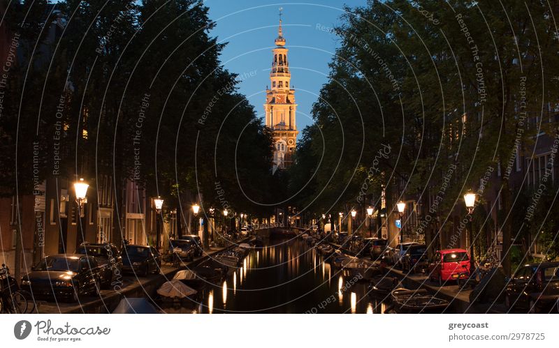 Amsterdamer Stadtbild bei Nacht. Szene mit Booten auf der mit Laternen gesäumten Gracht und Zuiderkerk, protestantische Kirche aus dem 17.