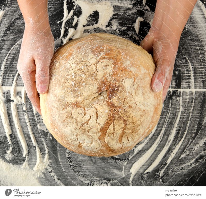 Frauenhände halten runde gebackene Brote. Teigwaren Backwaren Ernährung Tisch Küche Hand Holz Essen dunkel frisch groß natürlich oben braun schwarz Tradition