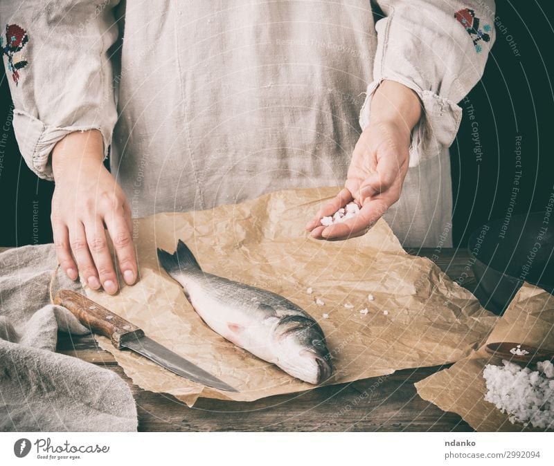 frischer ganzer Seebarschfisch auf braunem Papier liegend Fleisch Fisch Meeresfrüchte Kräuter & Gewürze Ernährung Tisch Küche Werkzeug Mensch Hand Tier Holz