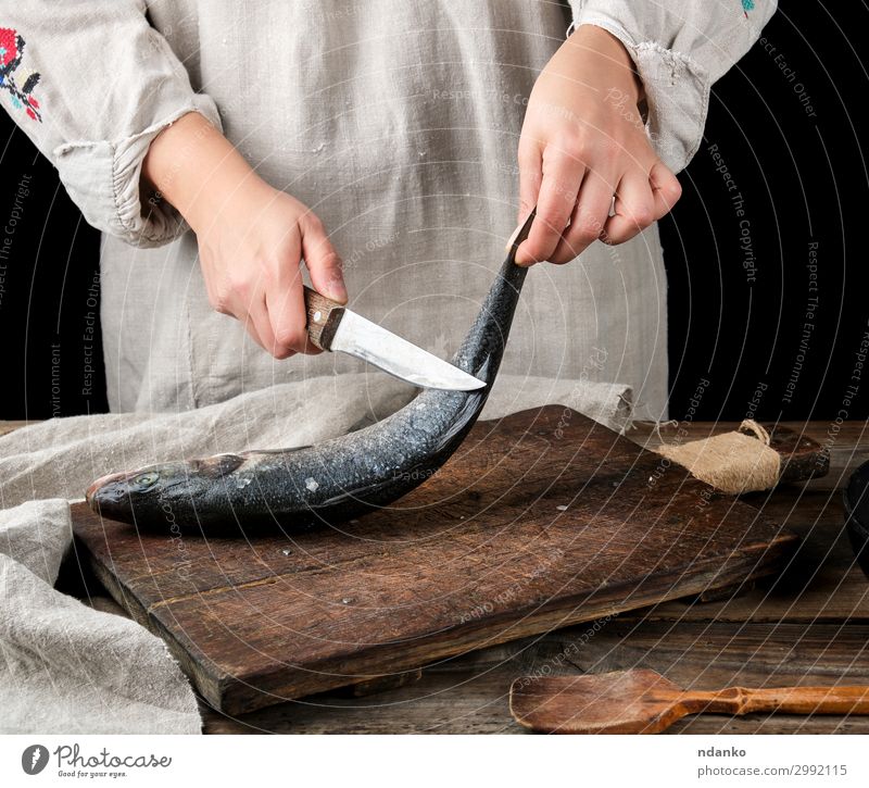 Frau in grauer Leinenkleidung reinigt den Fisch Seebarsch. Meeresfrüchte Messer Tisch Küche Werkzeug Erwachsene Hand Finger Holz alt machen frisch Sauberkeit