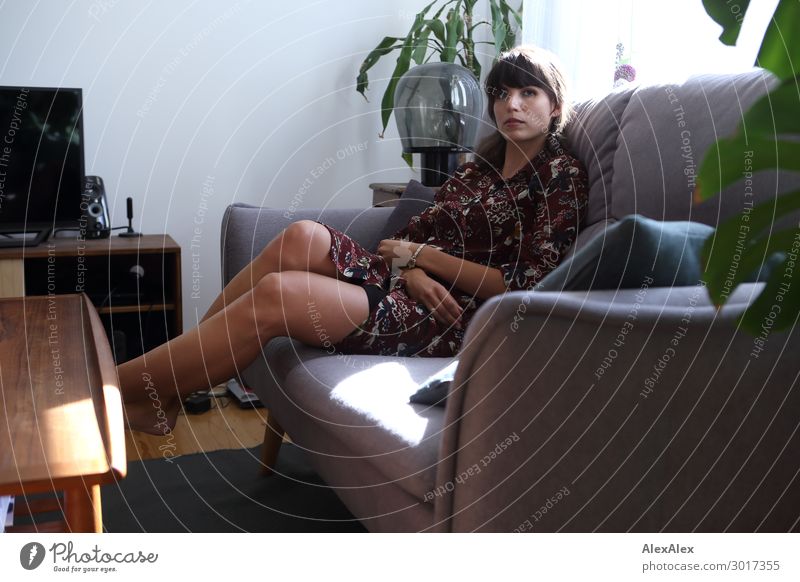 Junge Frau auf einer Couch im Wohnzimmer Lifestyle elegant Stil schön Wohlgefühl Zufriedenheit Erholung Wohnung Innenarchitektur Möbel Sofa Tisch Fernseher