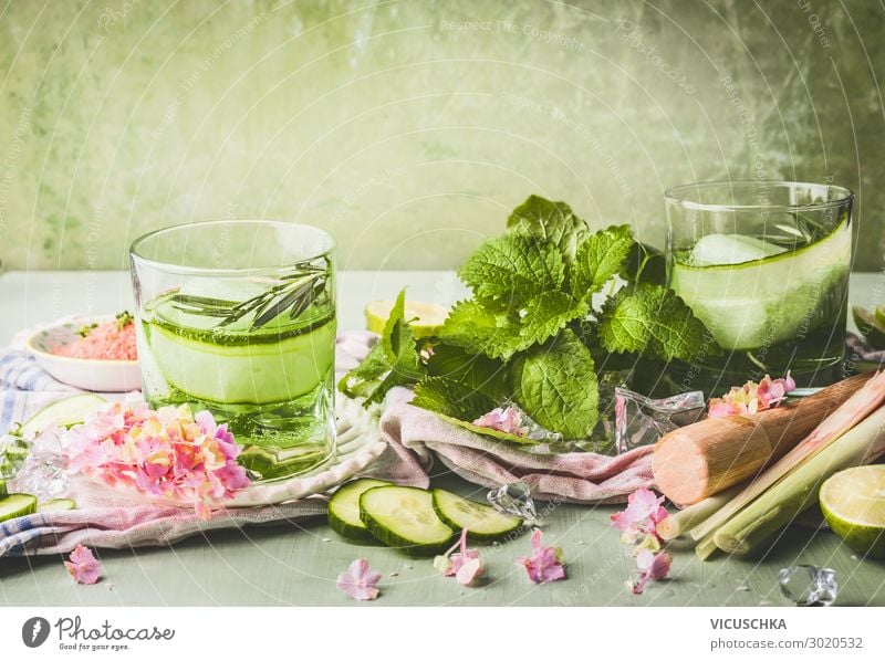 Klassen mit Gurkenlimonade oder Entgiftungswasser und Eiswürfel auf dem Tisch mit Zutaten. Grüne Farbe sommerliche Erfrischungsgetränke Zubereitung Salatgurke