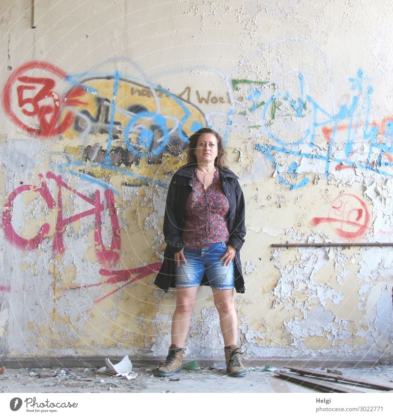Porträt einer Frau mit kurzen Jeans, bunter Bluse und dunkler Jacke steht vor einer maroden Wand mit Graffiti Mensch feminin Erwachsene 1 45-60 Jahre Gebäude