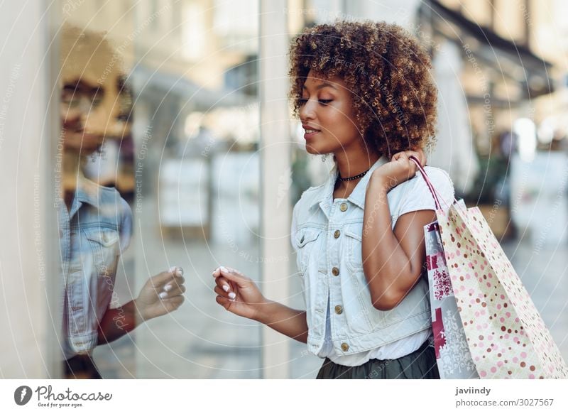 Junge schwarze Frau vor einem Schaufenster in einer Einkaufsstraße. Lifestyle kaufen Stil Glück schön Haare & Frisuren Mensch feminin Junge Frau Jugendliche